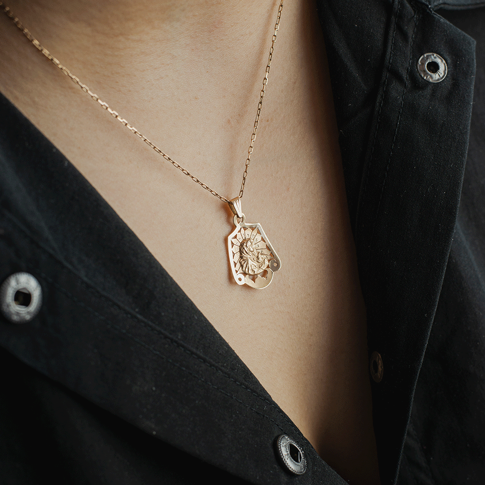 Colgante de la Virgen en oro de 18K llevado con una cadena sobre el pecho, con detalle de su figura en relieve y bordes calados.