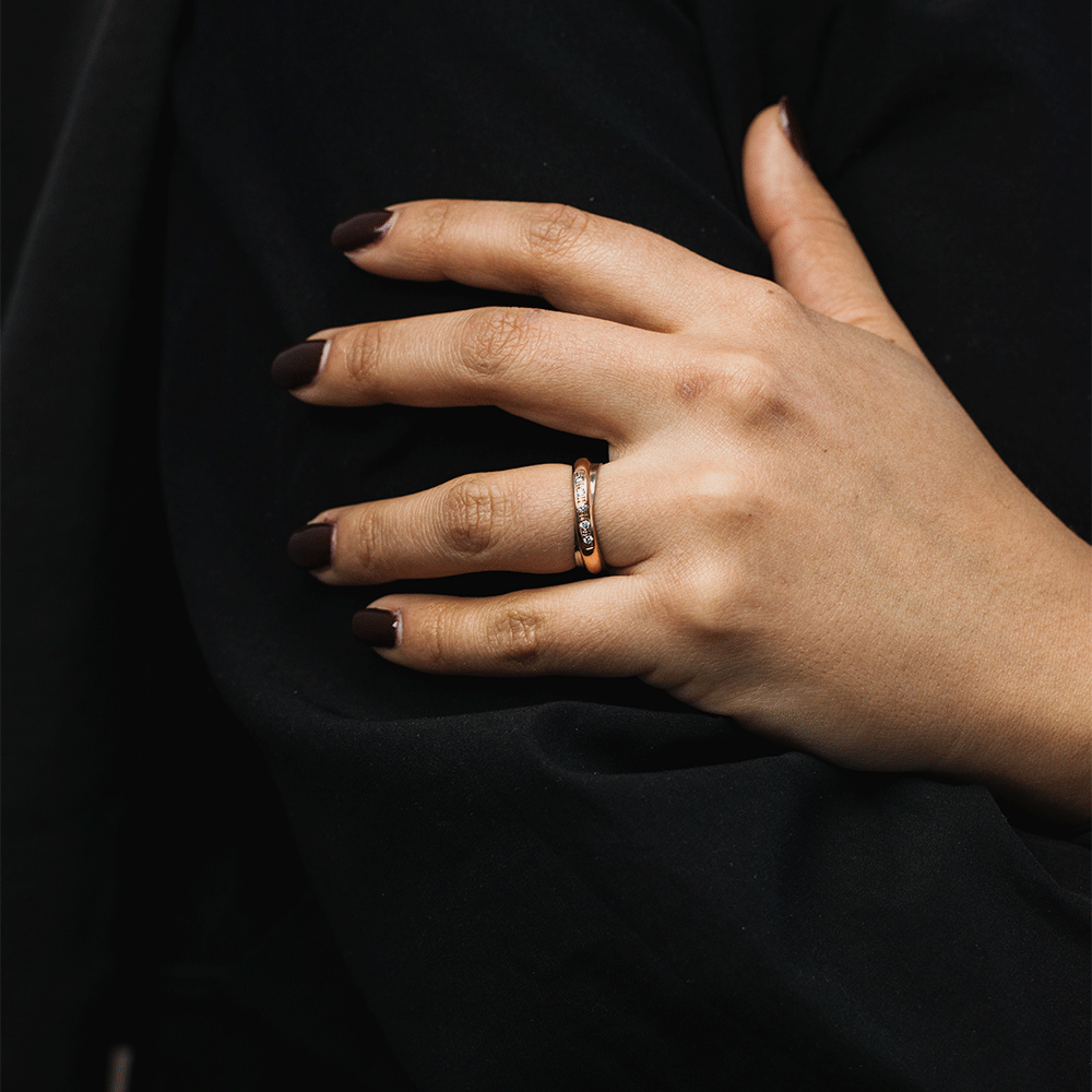 Anillo Aurore en oro bicolor de 18k con brillantes, puesto en el dedo anular de una mano sobre fondo negro.