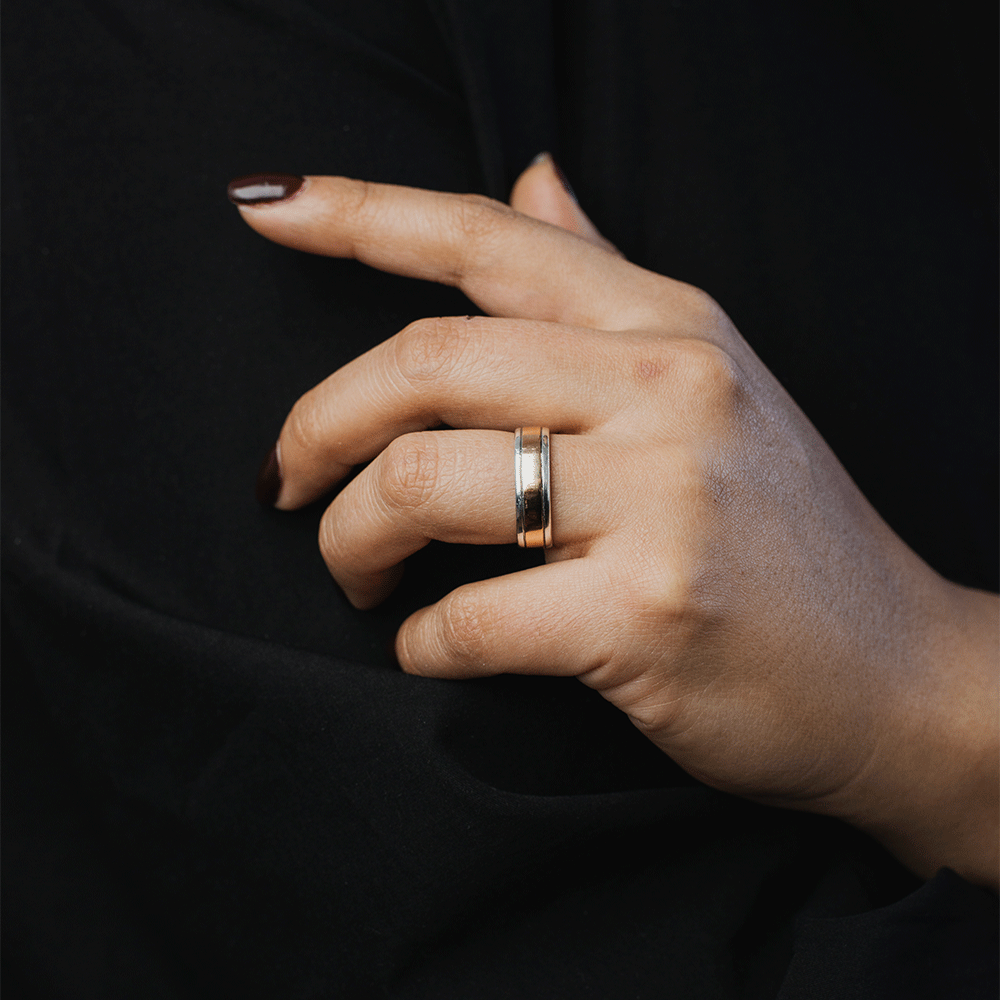 Anillo Éternité en plata y oro 18K, puesto en el dedo anular de una mano sobre fondo negro.