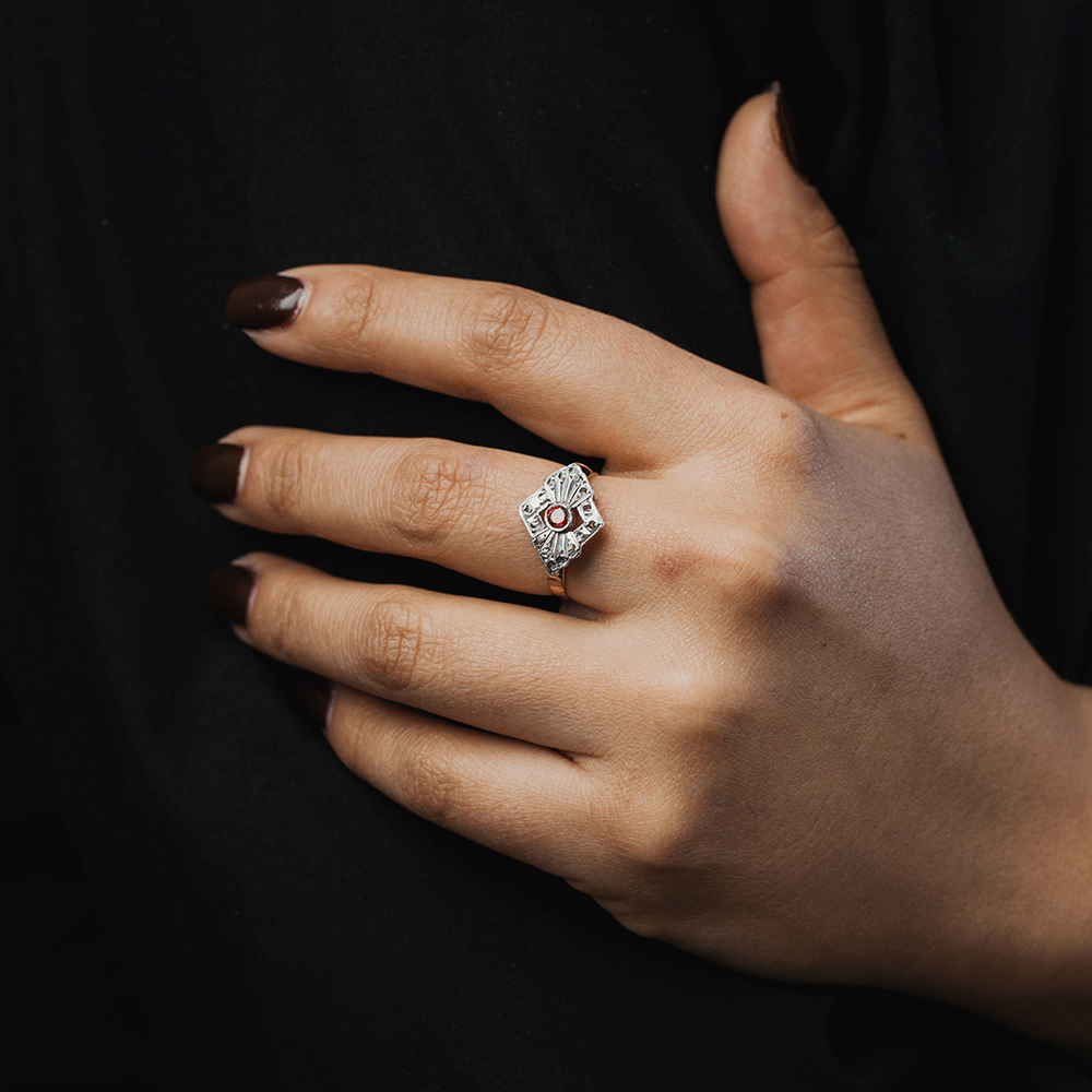 Anillo Victoria en plata y oro de 18K con rubí central y diamantes, puesto en una mano extendida sobre fondo negro.