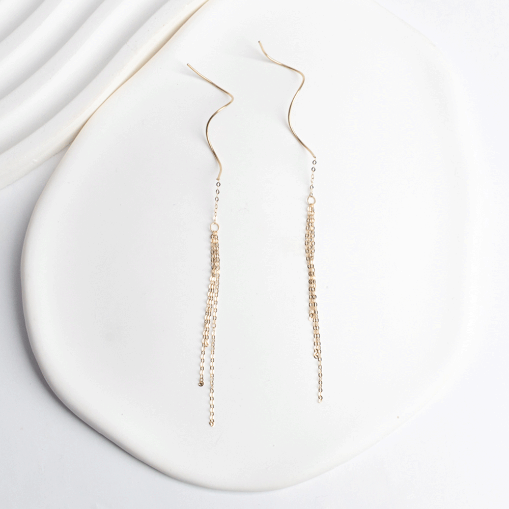 Aros Juliette en oro de 18K, con cadenas finas en cascada y detalles curvos, extendidos sobre fondo blanco