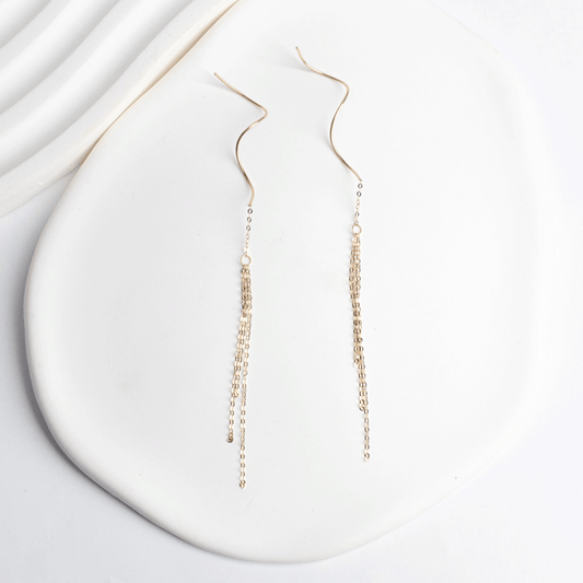 Aros Juliette en oro de 18K, con cadenas finas en cascada y detalles curvos, extendidos sobre fondo blanco