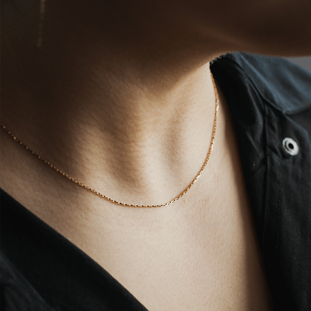 Cadena de eslabón tradicional en oro 18k, llevada al cuello con una blusa negra.