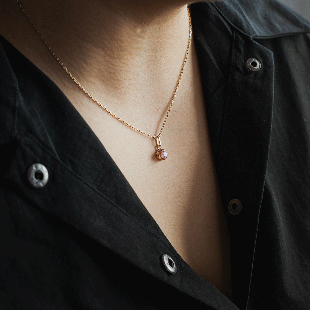 Colgante Punto de Luz Rosa de Francia en oro 18k, llevado con una cadena sobre el escote de una blusa negra.