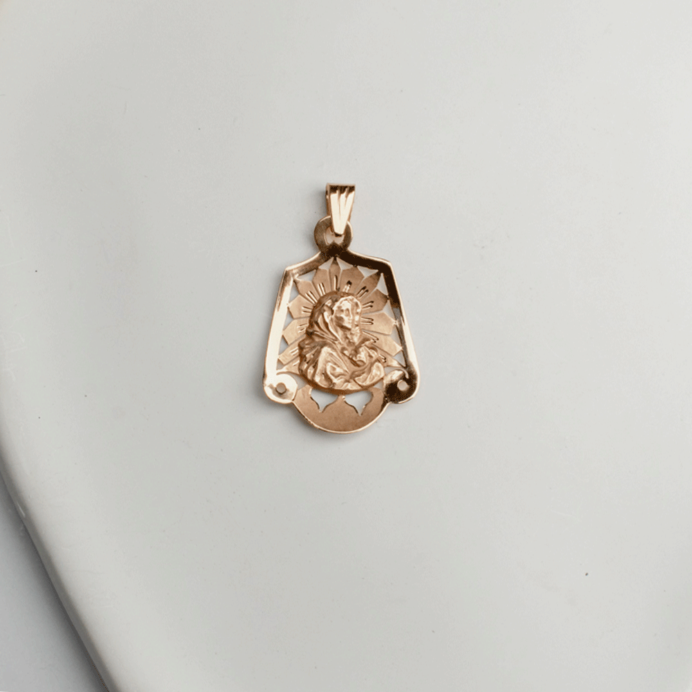 Colgante de la Virgen en oro de 18K, con figura en relieve, halo de rayos y detalles calados, sobre fondo blanco