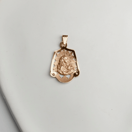 Colgante de la Virgen en oro de 18K, con figura en relieve, halo de rayos y detalles calados, sobre fondo blanco