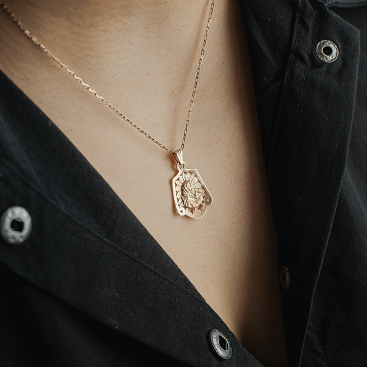 Colgante de la Virgen en oro de 18K llevado con una cadena sobre el pecho, con detalle de su figura en relieve y bordes calados.