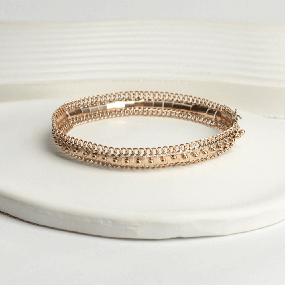 Pulsera Amaya en oro de 18k sobre una base clara, con detalles centrales en relieve y bordes de eslabones